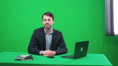 Stüdyoda oturan bir muhabir kameraya bakar, konuşur ve sunar bir haber programı yeşil bir arka plan, TV haber ajansları için bir şablon, iş yerinde bir gazeteci, kromakey.