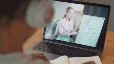 Genç Afrikalı kız bir masada dizüstü bilgisayar kullanarak ders çalışıyor, bir öğrenci uzaktan öğrendiği bir videoda öğretmeniyle konuşuyor, koronovirüs salgınının durumu hakkında eğitim görüyor, geri dönüyor.