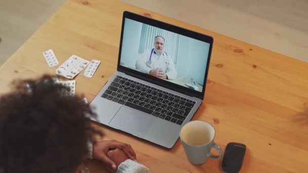 Mujer africana joven en aislamiento se comunica con un médico por videollamada utilizando una computadora portátil, una paciente consulta a un médico en línea mientras está en cuarentena, pandemia de coronovirus. — Vídeos de Stock