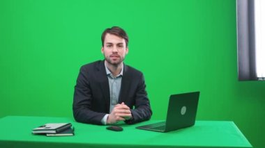 Stüdyoda oturan bir muhabir kameraya bakar, konuşur ve sunar bir haber programı yeşil bir arka plan, TV haber ajansları için bir şablon, iş yerinde bir gazeteci, kromakey.