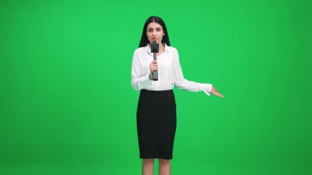 Vrouwelijke verslaggever in pak kijkt in de camera en spreekt in een microfoon op een groene achtergrond, een sjabloon voor tv-nieuwsagentschappen, journalist op het werk, chromakey. — Stockvideo
