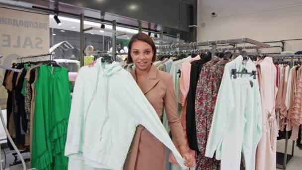 Genç Afrikalı kadın moda blogcusu bir giyim mağazasında yeni bir günlük kıyafet koleksiyonu sunuyor, kameraya bakıyor ve konuşuyor, sosyal ağda yayınlanıyor.. — Stok video