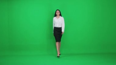 Takım elbiseli bir iş kadını yeşil bir zeminde yürüyor, gülümseyen bir kadın yaklaşıyor ve kameraya bakıyor, kroma anahtar şablonu..