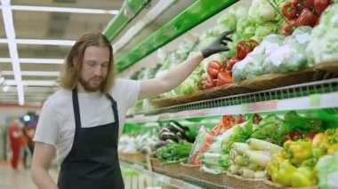Adam ürünleri raflara dolduruyor, genç adam organik bir mağazanın rafına kırmızı biber koyuyor, bakkalda çalışıyor..