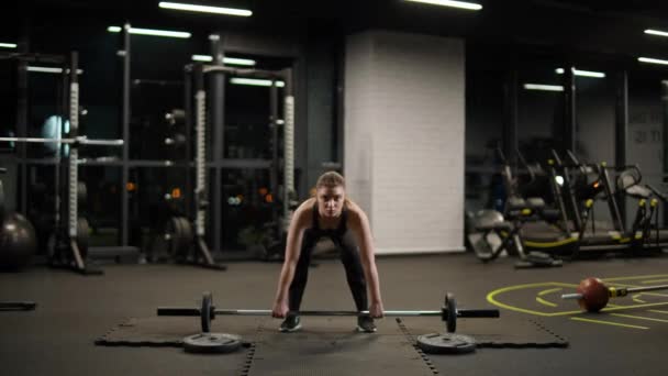 Atletisch vrouwtje doet oefeningen met lange halter, tilt lange halter en doet zware gewichten training in de sportschool. — Stockvideo