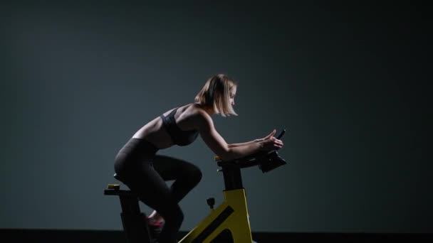 Cycle training, giovane donna è impegnata nel fitness su una spin bike, esegue un allenamento di resistenza aerobica sul simulatore in palestra. — Video Stock