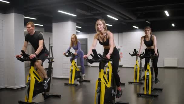 Grupa ludzi trenuje na rowerach spinningowych, wykonuje trening wytrzymałościowy aerobowy na symulatorach na siłowni, trening rowerowy. — Wideo stockowe