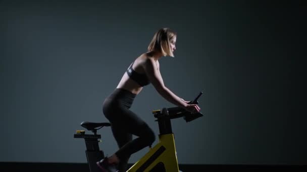 Cycle training, giovane donna è impegnata nel fitness su una spin bike, esegue un allenamento di resistenza aerobica sul simulatore in palestra. — Video Stock