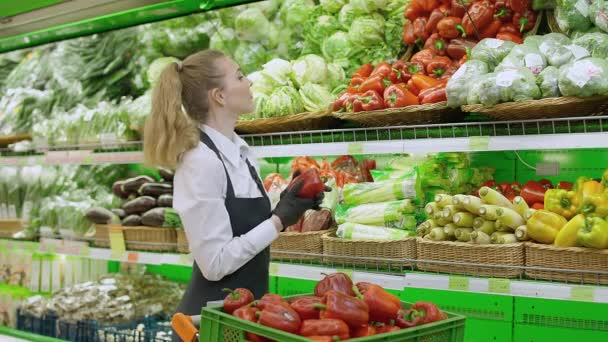 Mujer pone pimiento rojo en un estante en una tienda orgánica, mujer joven repone productos en los estantes, trabaja en una tienda de comestibles. — Vídeos de Stock