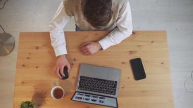 Adam bir masada oturuyor ve dizüstü bilgisayar kullanıyor, internette geziniyor, online mağazaları ziyaret ediyor, karantinada zaman geçiriyor, üst görünümde..