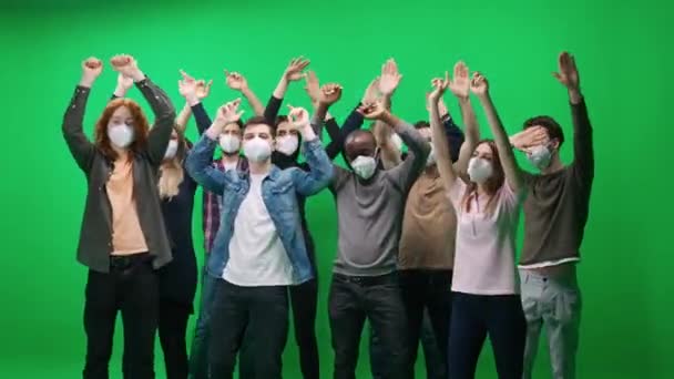 Multitud de personas de diferentes edades bailando en un concierto, personas con máscaras médicas protectoras, fans en un concierto de música, bailan y balancean sus brazos sobre un fondo verde, una plantilla de cromakey, evento — Vídeo de stock