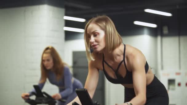 Wellness, vrouwelijke training op een spinfiets, twee vrouwen doen aeroob uithoudingstraining op de simulatoren in de sportschool, fietstraining. — Stockvideo