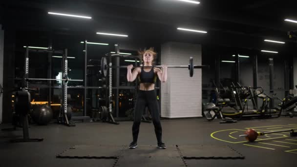 Atletisch vrouwtje doet oefeningen met lange halter, tilt lange halter en doet zware gewichten training in de sportschool. — Stockvideo