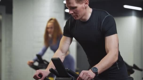 Mężczyzna i kobieta trening na rowerach spinningowych, wykonuje trening wytrzymałościowy aerobowy na symulatorach w siłowni, trening rowerowy. — Wideo stockowe