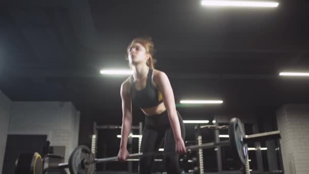 Jonge vrouw voert een deadlift, het doen van oefeningen met lange halter, liften lange halter en doet gewichtstraining in de sportschool. — Stockvideo