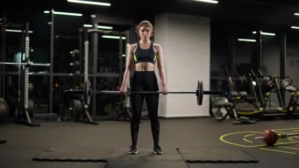 Vrouw voert een deadlift, het doen van oefeningen met lange halter, liften lange halter en doet gewichtstraining in de sportschool. — Stockvideo