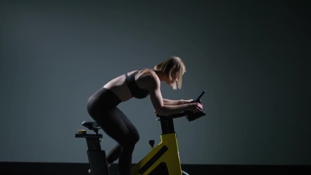 Giovane donna è impegnata in una moderna spin bike, esegue un allenamento di resistenza aerobica sul simulatore in palestra. — Video Stock