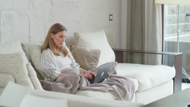 Weibchen sitzt zu Hause auf der Couch und arbeitet mit Laptop, Manager auf Fernarbeit während der Selbstisolierung in Quarantäne, Frau macht ein gutes Geschäft, positive Emotionen. — Stockvideo