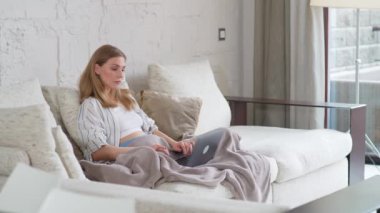 Kadın evdeki kanepede oturuyor ve dizüstü bilgisayar kullanıyor. Karantinada kendini izole ederken uzaktan kumandayla çalışıyor. Rutin iş..