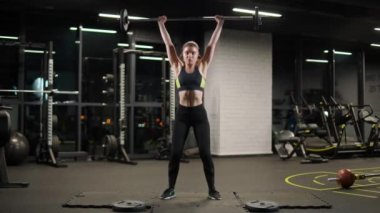 Güçlü atletik kadın halterle egzersiz yapıyor, halteri kaldırıyor ve spor salonunda ağırlık çalışması yapıyor..