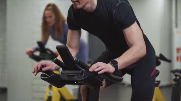 Mężczyzna i kobieta trening na rowerach spinningowych, wykonuje trening wytrzymałościowy aerobowy na symulatorach w siłowni, trening rowerowy. — Wideo stockowe