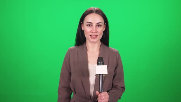 Reportera de traje mira a la cámara y habla en un micrófono sobre un fondo verde, plantilla para agencias de noticias de televisión, periodista en el trabajo, chromakey. — Vídeos de Stock