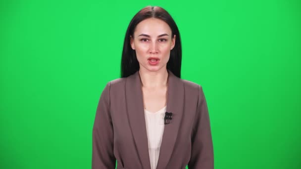 Mujer reportera de traje mira a la cámara y habla en un micrófono sobre un fondo verde, plantilla para agencias de noticias de televisión, periodista en el trabajo, chromakey. — Vídeos de Stock