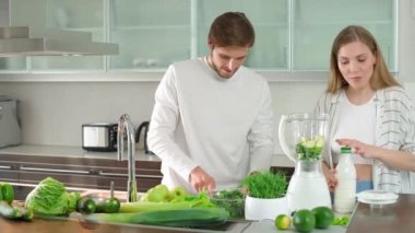 Vejetaryenlik, genç bir çift mutfakta meyve püresi hazırlar, erkek ve kadın yeşil sebzeleri karıştırıcıya koyar..