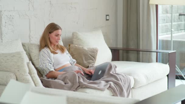 Donna si siede sul divano a casa e lavora con un computer portatile, manager su un lavoro a distanza durante l'auto-isolamento in quarantena, la donna fa un buon affare, emozioni positive. — Video Stock