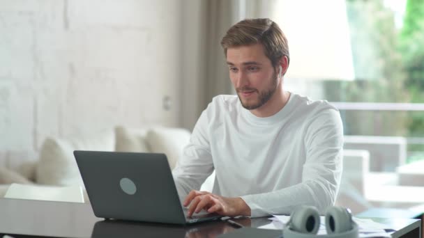 Homme caucasien joyeux assis à la maison sur le bureau et travaille à l'aide d'un ordinateur portable, gestionnaire financier sur un travail à distance pendant l'auto-isolement en quarantaine, un homme fait une bonne affaire, émotions positives. — Video