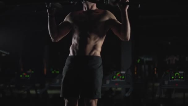 Wellness, atletický muž provádí pull-up na horizontálním baru, silový trénink v tělocvičně v noci, kinematografické světlo. — Stock video