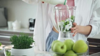 Kadın mutfakta meyve püresi hazırlar, kadın yeşil sebzeleri karıştırıcıya koyar ve karıştırır..