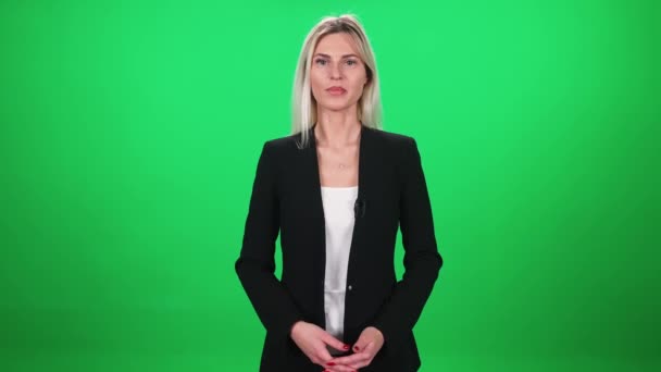 Mujer reportera de traje mira a la cámara y habla en micrófono lavalier, mujer sobre un fondo verde, plantilla para agencias de noticias de televisión, periodista en el trabajo, chromakey. — Vídeos de Stock