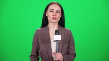 Takım elbiseli kadın muhabir kameraya bakar ve yeşil arka plandaki bir mikrofona konuşur, TV haber ajansları için şablon, iş yerindeki gazeteci, kromakey.