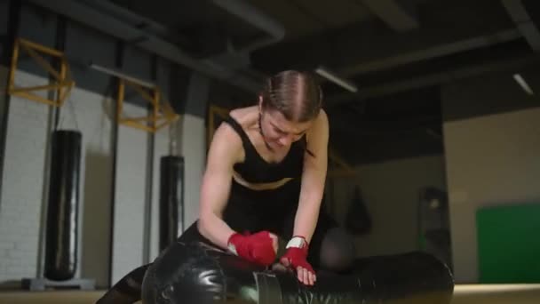 Kickboxing, lutador mulher agressiva treina seus socos, bate um saco de perfuração enquanto deitado no chão, dia de treinamento no ginásio de boxe, corpo de ajuste de força, a menina bate rápido. — Vídeo de Stock