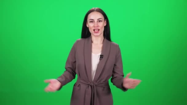 Female reporter in suit looks into the camera and speaks into a lavalier microphone on a green background, template for TV news agencies, journalist at work, chromakey. — Stock Video