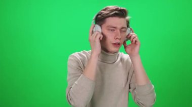 Genç bir adamın portresi, bir müzik aşığı kablosuz kulaklıkla müzik dinler ve yeşil bir arka planda şarkı söyleyerek dans eder..