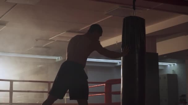 Kickboxing, atletyczny bokser trenuje uderzenia, bije worek treningowy, trenuje umiejętności kopania na siłowni bokserskiej. — Wideo stockowe