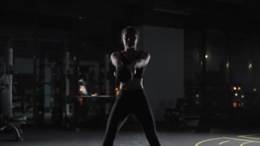 Kafkasyalı atletik kadın kettlebell egzersizleri yapıyor, ağırlık kaldırıyor ve spor salonunda kettlebell Crossfit antrenmanı yapıyor, dramatik ışıklandırma..