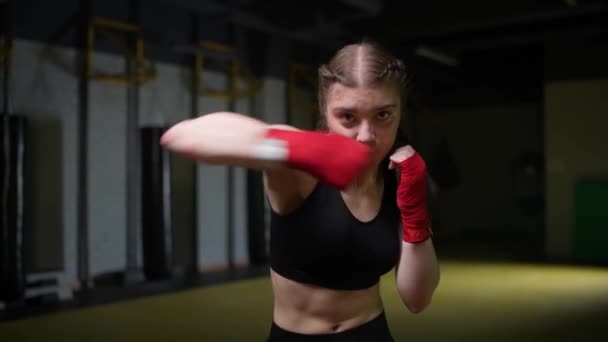 Kobieta zawodniczka trenuje ciosy, trening w siłowni bokserskiej, młoda kobieta patrzy w kamerę i trenuje serię ciosów, 4k zwolniony ruch. — Wideo stockowe