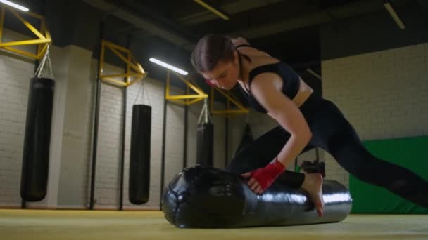 Kickboxing, επιθετική γυναίκα μαχητής εκπαιδεύει γροθιές του, κτυπά ένα σάκο του μποξ, ενώ βρίσκεται στο πάτωμα, ημέρα κατάρτισης στο γυμναστήριο πυγμαχίας, δύναμη ταιριάζει σώμα, 4k αργή κίνηση. — Αρχείο Βίντεο