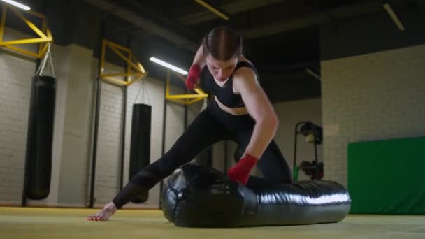 Donna aggressiva combattente allena i pugni, batte un sacco da boxe mentre sdraiato sul pavimento, giornata di allenamento in palestra di pugilato, corpo in forma di forza, 4k rallentatore. — Video Stock