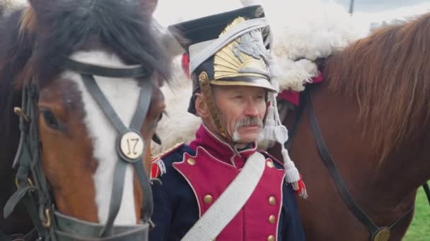 Портрет взрослого гусара в средневековом костюме, солдата, стоящего рядом с лошадью в поле, крупным планом, 4К замедленной съемки. — стоковое видео