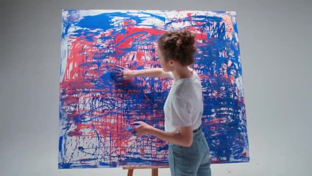 Vrouwelijke kunstenaar tekent met haar handen op een groot doek in een witte kamer, een getalenteerde kunstenaar trekt een kleur abstractie, moderne kunst in olieverf. — Stockvideo