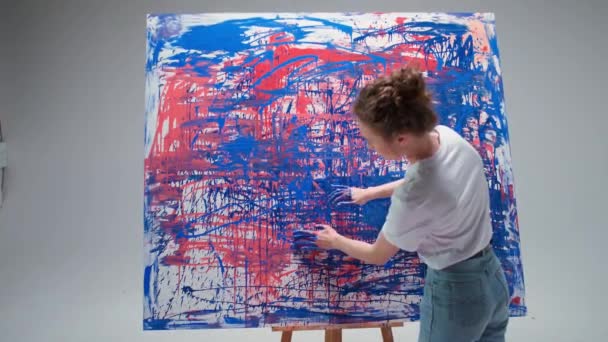 Arte moderna, jovem artista feminina desenha com as mãos em uma grande tela em uma sala branca, um artista talentoso desenha uma abstração de cor, pintura a óleo. — Vídeo de Stock