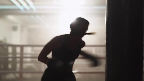 Vista borrosa, mujer luchadora entrena sus golpes, supera un saco de boxeo, día de entrenamiento en el gimnasio de boxeo, cuerpo de fuerza en forma, la mujer golpea rápido. — Vídeo de stock