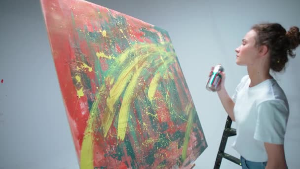 若い女性アーティストはスプレーで描き、白い部屋の大きなキャンバスにペイントし、才能のあるアーティストはカラー抽象化、 4kスローモーションを描きます. — ストック動画