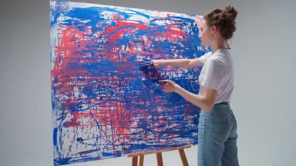Γυναίκα καλλιτέχνης ζωγραφίζει με τα χέρια της σε ένα μεγάλο καμβά σε ένα λευκό δωμάτιο, ένας ταλαντούχος καλλιτέχνης αντλεί ένα χρώμα αφαίρεσης, σύγχρονη τέχνη στη ζωγραφική πετρελαίου. — Αρχείο Βίντεο