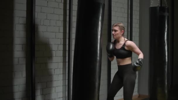 Athletische Kämpferin trainiert ihre Schläge, schlägt einen Boxsack, Kickbox-Trainingstag in der Boxhalle, 4k Zeitlupe.