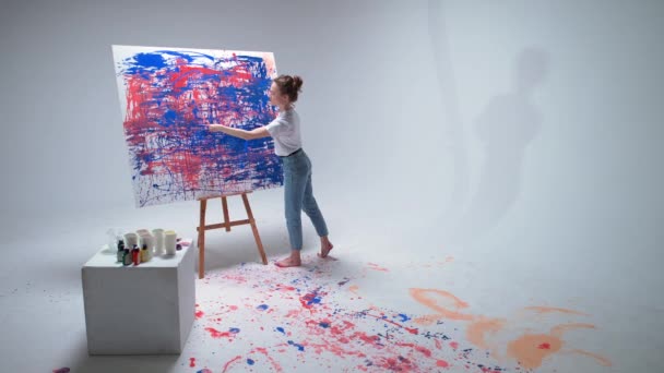 Γυναίκα καλλιτέχνης ζωγραφίζει με τα χέρια της σε ένα μεγάλο καμβά σε ένα λευκό δωμάτιο, ένας ταλαντούχος καλλιτέχνης αντλεί ένα χρώμα αφαίρεσης, σύγχρονη τέχνη στη ζωγραφική πετρελαίου. — Αρχείο Βίντεο
